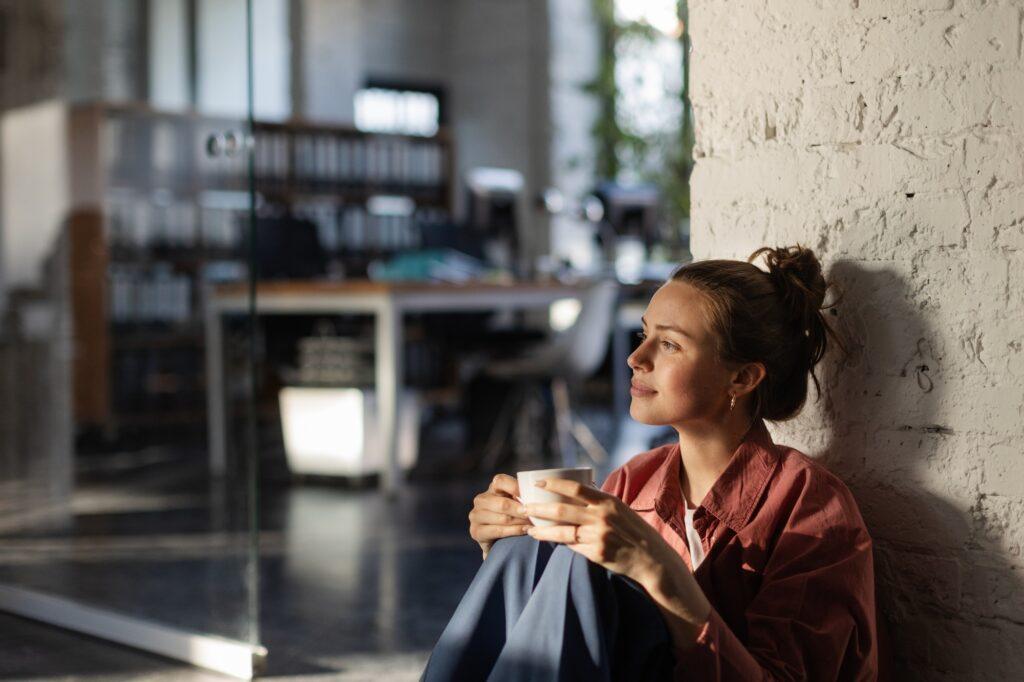 Happy female business owner in her own office drinking coffee and watching sunset.